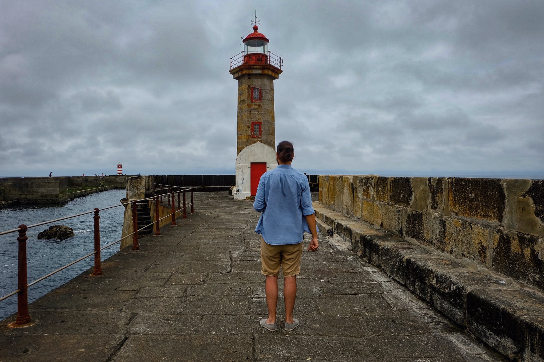 man standing on stone bridge with beacon